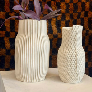 Two textured ceramic vases with a plant against a checkered background