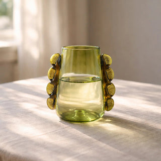 Green glass vase with decorative handles on a textured surface