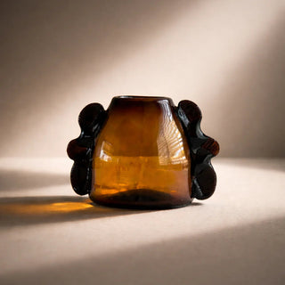 Amber glass vase with decorative handles on a neutral background