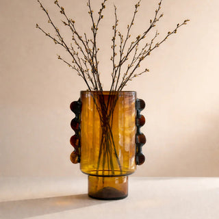 Amber glass vase with decorative elements holding branches on a beige background