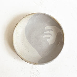 A round handmade ceramic plate with a matte finish, featuring a light gray and off-white abstract design on the inside
