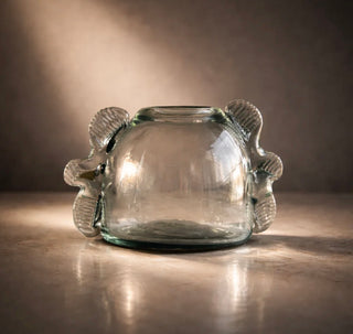 Clear glass candle holder with fish designs on a reflective surface