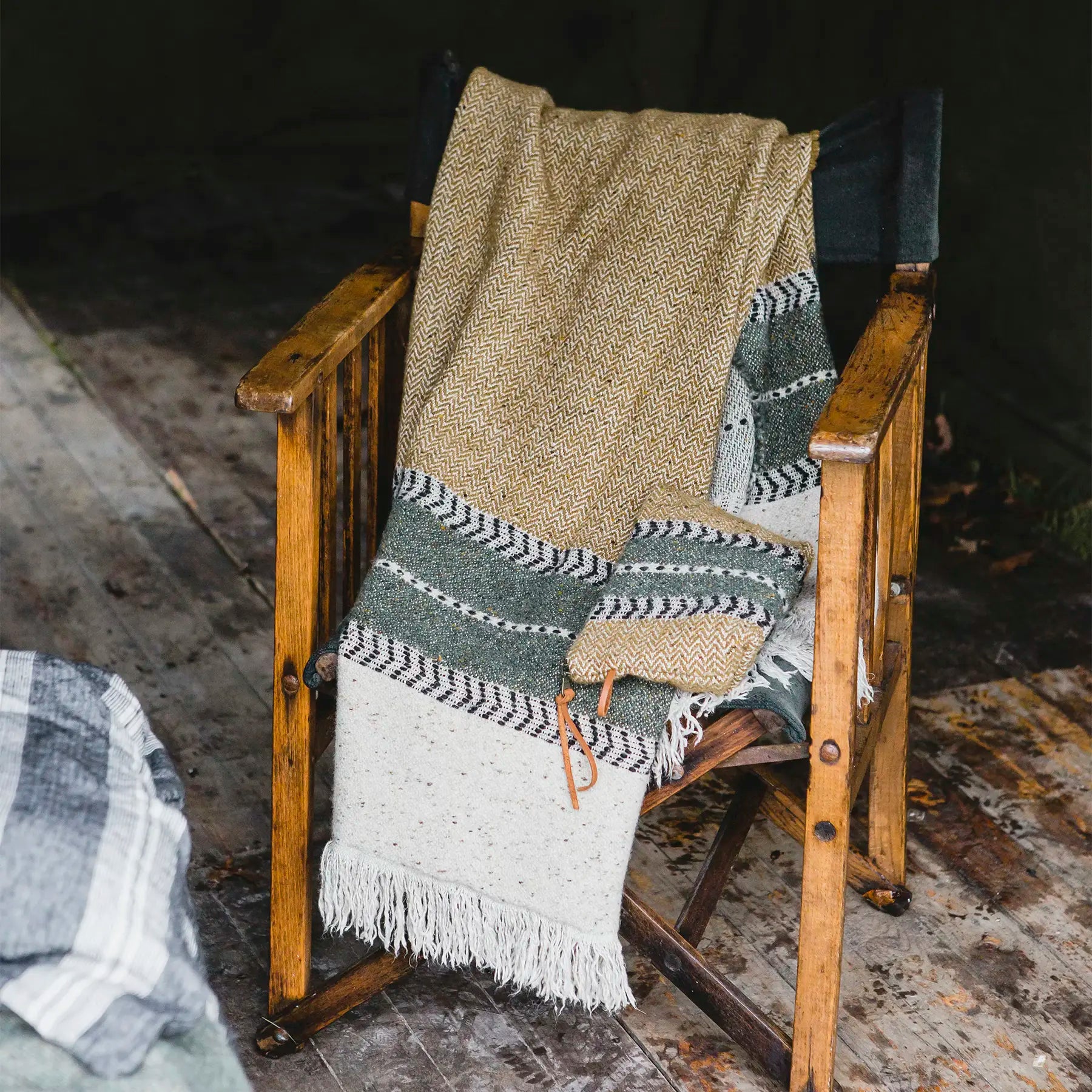 Woven blanket draped over a wooden chair on a rustic wooden floor