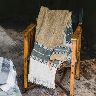 Woven blanket draped over a wooden chair on a rustic wooden floor