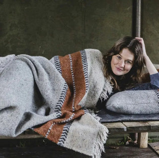 Woman lying on a wooden bench with a blanket and pillow