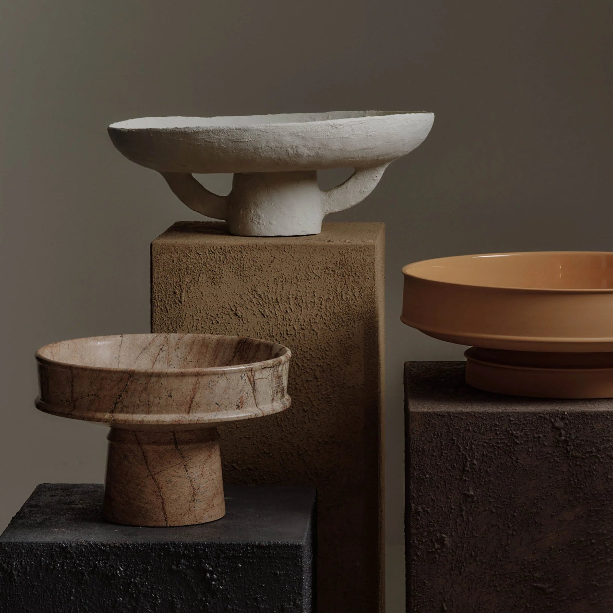 Three stone bowls of different sizes on elevated platforms against a dark background