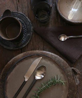 Dining table setting with ceramic plates, cutlery, and a napkin on a wooden surface.