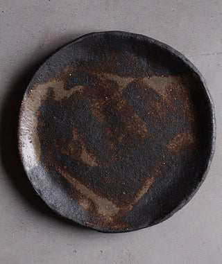 Dark ceramic plate with textured surface on a gray background
