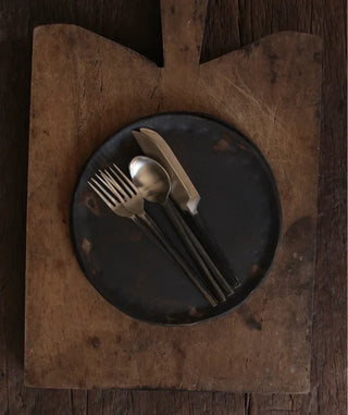 Dark plate with silverware on a wooden cutting board