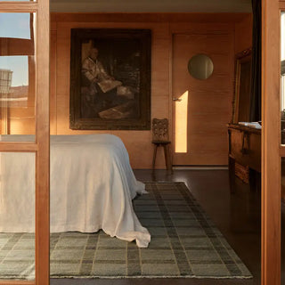Room interior with a bed draped in white sheets, wooden furniture, and a painting on the wall.
