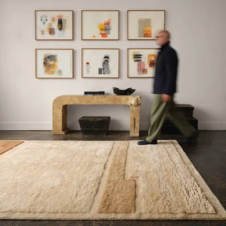 Man walking past a decorative console table with framed art on the wall in a room with a textured rug.
