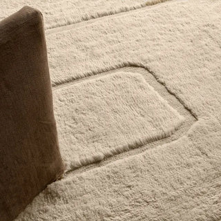 Close-up of a textured beige carpet with a brown chair corner.