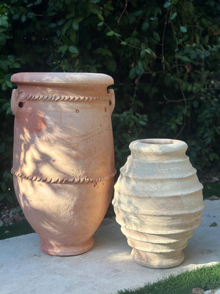 Two terracotta pots on a stone surface with a green outdoor background