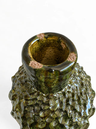 A close-up of a textured ceramic vase with a glossy, organic, bumpy surface in olive green and dark brown glazes, showing the interior and a small section of the rim against a white background.