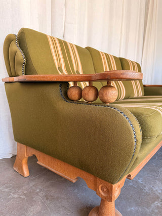 Green upholstered sofa with wooden armrest and legs against a white curtain 