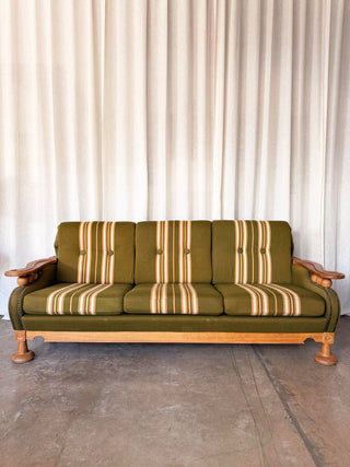 Green upholstered sofa with wooden armrest and legs against a white curtain 