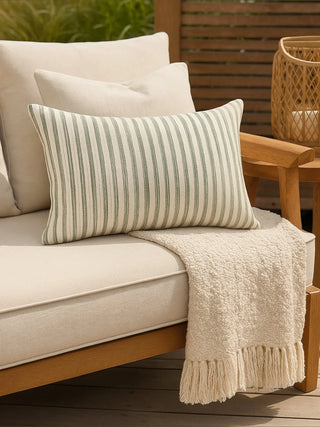 Striped pillow on a beige outdoor sofa with a wooden armchair in the background.