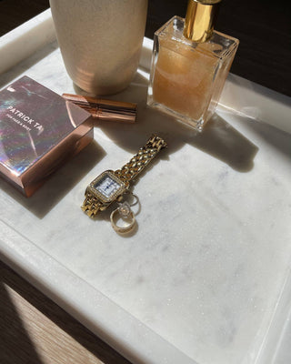 Gold watch, perfume bottle, and makeup item on a marble tray