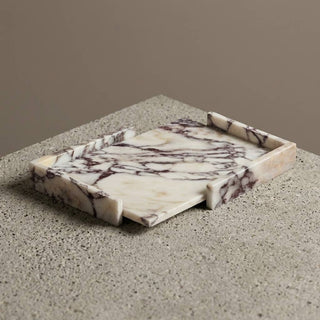 A rectangular marble serving tray with a cream and white base and dark brown veining, shown on a speckled stone surface against a warm taupe background.