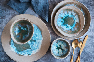 Set of ceramic plates with blue and green glaze on a gray surface with cutlery.