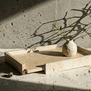 A rectangular light beige stone tray with a small pull-out drawer, styled on a textured stone surface with a small ceramic vase and dried branches under dramatic natural shadows.