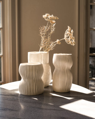 Set of Three Cream colored handmade porcelain ceramic flower vases with organic ribbed patterns sitting on marble table